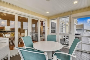 A covered outdoor dining area with a round table and chairs, large windows, and a view of the surrounding buildings.