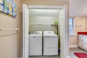 Une buanderie équipée de deux machines à laver et de deux sèche-linge à chargement frontal, tous deux blancs, d’un porte-serviettes blanc et d’une étagère verte sur laquelle se trouve un sac.