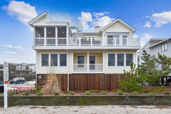 A two-story house with a balcony, a wooden fence, and a sandy ground.