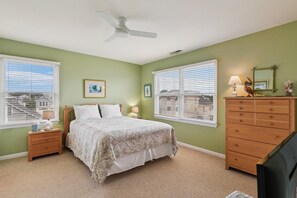A bedroom with a bed, nightstands, a dresser, a ceiling fan, and large windows with blinds.