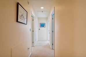 A hallway with doors on both sides, a framed picture on the left wall, and a framed picture on the right wall.