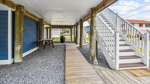Un espacio al aire libre techado con piso de madera, una mesa de picnic y una escalera que lleva a un edificio.