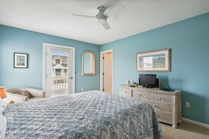 A bedroom with a bed, a television on a dresser, and a ceiling fan.