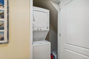 A laundry room with a stacked washer and dryer, a door, and a wall-mounted picture frame.