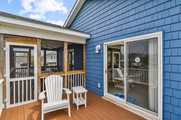 A blue house with a wooden deck, a white chair, and a glass door.