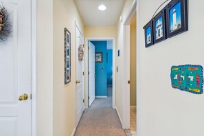 A hallway with white doors, a blue door at the end, and a wall with framed pictures and a decorative fish-themed switchboard.