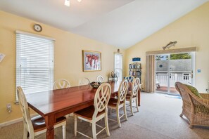 A dining area with a wooden table and chairs, a bookshelf, and a view of the outdoors through a sliding glass door.
