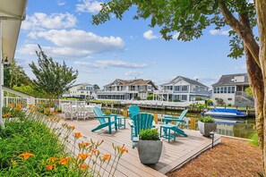 A wooden deck with chairs and a potted plant, overlooking a calm water body and houses.