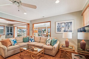 A living room with a sectional sofa, glass coffee table, and a ceiling fan.