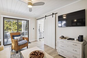 A modern living room with a large TV, a dining area, and a sliding door leading to a balcony.