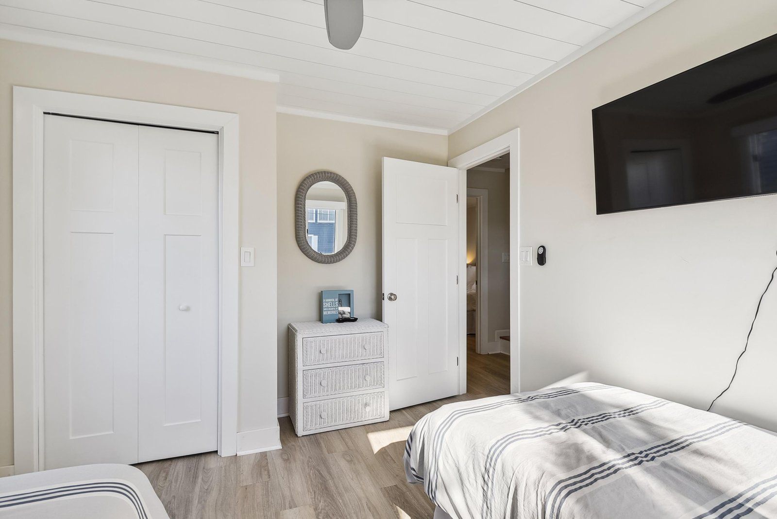Um quarto com cama, cômoda, espelho e televisão na parede.