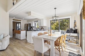 A modern kitchen with white cabinetry, a central island, and a dining area with a white table and wicker chairs.