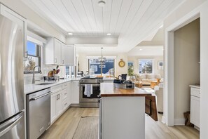A modern kitchen with stainless steel appliances, a central island, and a view to the living area.
