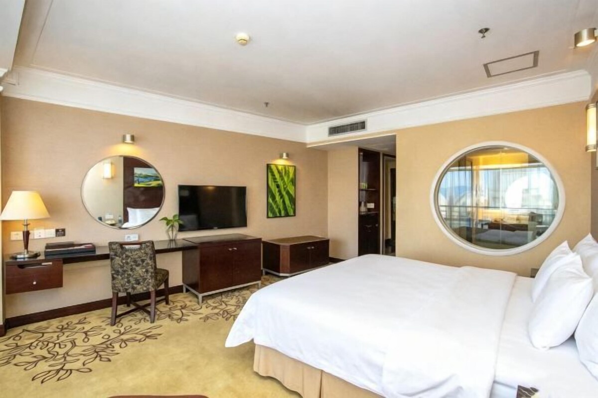 A hotel room with a bed, desk, chair, television, and a large window.