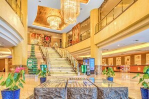 A spacious lobby with a grand staircase, a reception desk, and decorative potted plants.