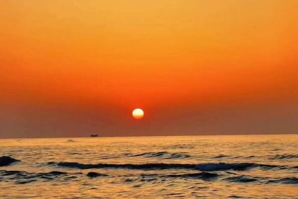 A sunset over the ocean with a boat in the distance.