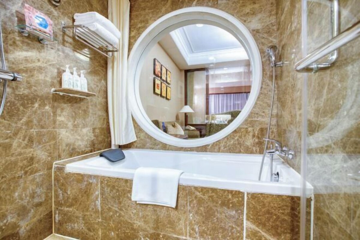 A bathroom with a marble wall, a round mirror, a white sink, and a shower area.