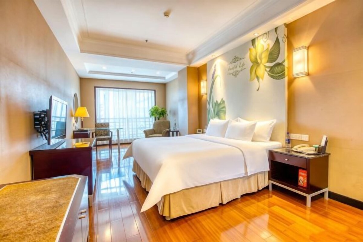 A hotel room with a large bed, a desk, a chair, a TV, and a window with a view.