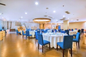 A banquet hall with round tables and blue chairs, a staircase, and a decorative ceiling light.