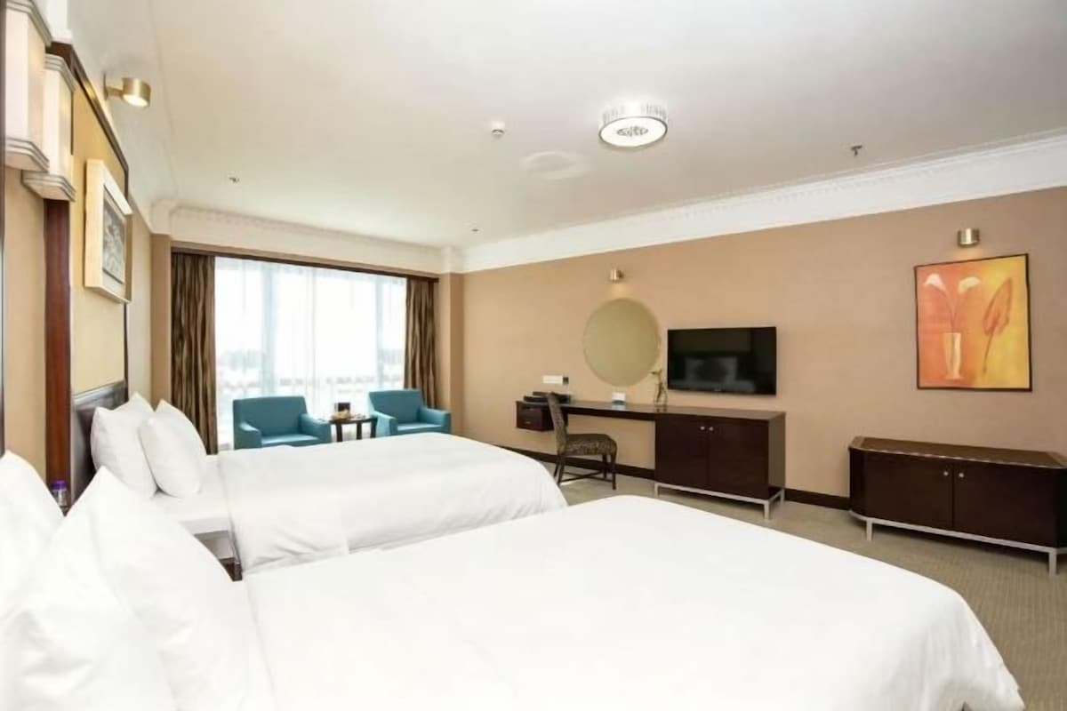 A hotel room with two beds, a desk, a chair, a TV, and a window with curtains.