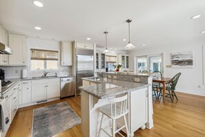 A modern kitchen with white cabinets, stainless steel appliances, granite countertops, and pendant lighting. - Coastal Bliss Nestled in Bethany Beach: Oceanside, Elevator, Sleeps 16 (South Bethany)