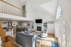 A spacious living area with a high ceiling, a fireplace, a television, and a dining area with chairs and a table. - Coastal Bliss Nestled in Bethany Beach: Oceanside, Elevator, Sleeps 16 (South Bethany)