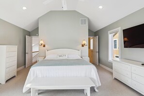 A bedroom with a large bed, bedside tables, a dresser, a TV, and a window.