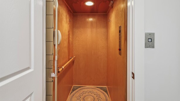 An elevator with wooden walls, a handrail, and a patterned mat at the bottom. - Coastal Bliss Nestled in Bethany Beach: Oceanside, Elevator, Sleeps 16 (South Bethany)