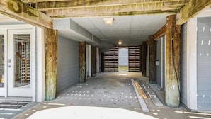 A hallway with wooden beams, a concrete floor, and a view of a gated area in the distance. - Coastal Bliss Nestled in Bethany Beach: Oceanside, Elevator, Sleeps 16 (South Bethany)