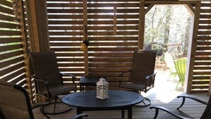 A covered patio area with a round table and four chairs, a lantern, and a wooden fence. - Spacious Bayside 5 Bedroom in Bethany Beach! (South Bethany)
