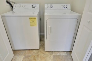 A laundry room with two stacked washers and dryers, a yellow energy guide sticker, and a tiled floor.