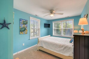 A bedroom with a bed, two windows with blinds, a ceiling fan, a starfish decoration, and a turtle painting on the wall.