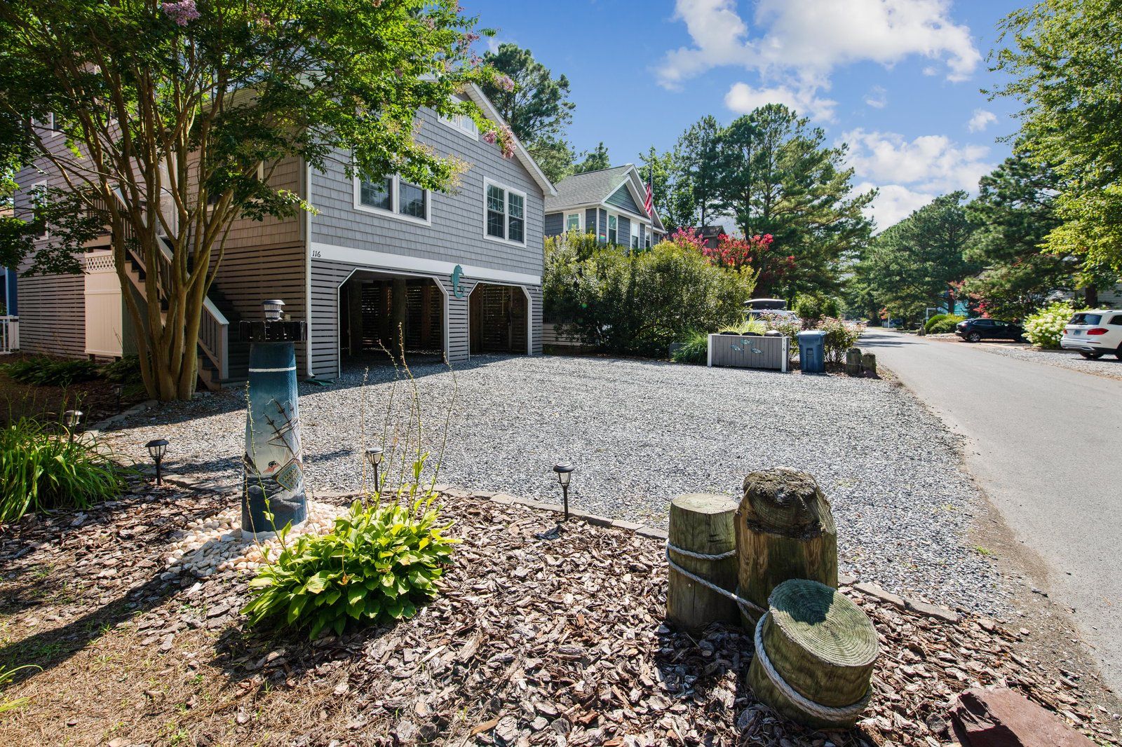 A residential driveway with a gravel surface, a wooden fence, and a house with a garage.