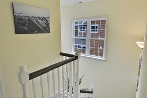 Un escalier avec des balustrades blanches et une main courante sombre, une fenêtre donnant sur un bâtiment en briques et un tableau encadré accroché au mur.