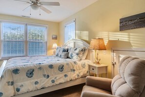 Quarto com cama, cadeira, mesa de cabeceira, abajur e ventilador de teto.
