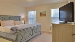 A bedroom with a bed, a TV on a cabinet, and two windows with blinds. - Spacious Bayside 5 Bedroom in Bethany Beach! (South Bethany)