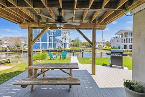 A wooden deck with a table and chairs, overlooking a water body and buildings. - Waterfront 4 Bedroom, 3 Bathroom, Bethany Beach Home With Canal Views! (South Bethany)