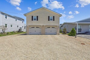 A two-story house with a double garage, a gravel driveway, and a small tree in the front yard. - Waterfront 4 Bedroom, 3 Bathroom, Bethany Beach Home With Canal Views! (South Bethany)