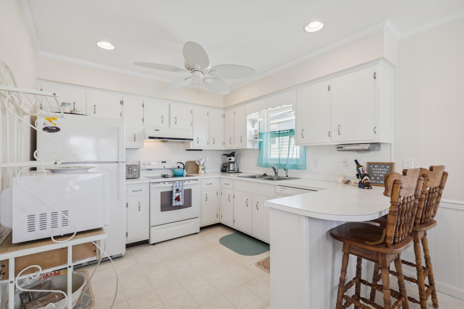 A kitchen with white cabinets, a stove, a sink, and a ceiling fan.