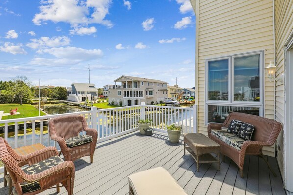 A deck with wicker furniture, a white railing, and a view of a residential area.
