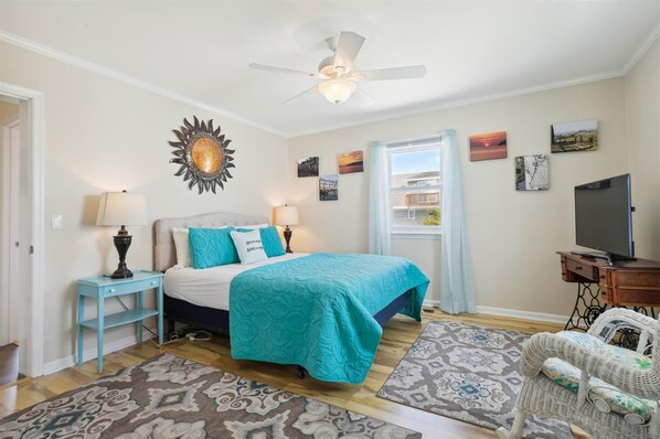 A bedroom with a bed, nightstands, a ceiling fan, artwork, a TV, and a wicker chair. - Waterfront 4 Bedroom, 3 Bathroom, Bethany Beach Home With Canal Views! (South Bethany)
