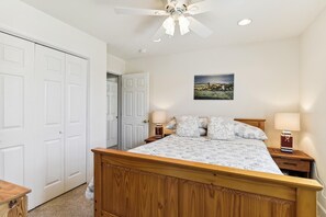 A bedroom with a wooden bed, two bedside tables with lamps, a ceiling fan, and a door leading to another room. - Bayside South Bethany Home (South Bethany)