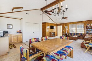 A dining area with a wooden table and colorful upholstered chairs, a ceiling fan, and a chandelier. - Bayside South Bethany Home (South Bethany)