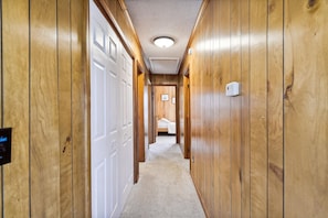 A hallway with wooden walls, a carpeted floor, and a bed in the distance. - Bayside South Bethany Home (South Bethany)