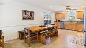 A kitchen with wooden cabinets, a stainless steel refrigerator, and a dining area with a wooden table and bench. - Bayside South Bethany Home (South Bethany)