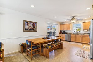 A kitchen with wooden cabinets, a stainless steel refrigerator, and a dining area with a wooden table and bench. - Bayside South Bethany Home (South Bethany)
