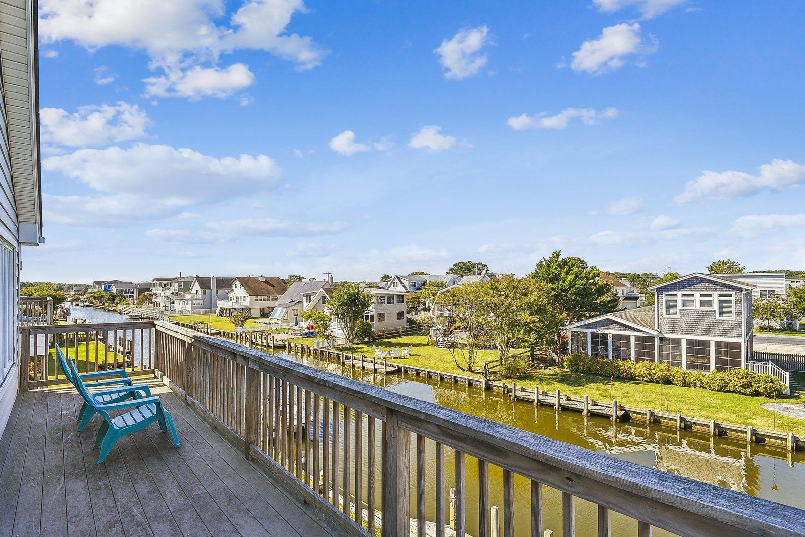 A waterfront property with a wooden deck, a small boat dock, and a view of the water and neighboring houses.