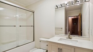 A bathroom with a glass shower enclosure, a white sink, and a mirror with lights. - Bayside South Bethany Home (South Bethany)