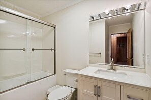 A bathroom with a glass shower enclosure, a white sink, and a mirror with lights. - Bayside South Bethany Home (South Bethany)