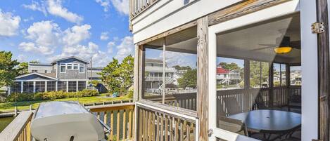 A deck with a grill and a table, overlooking a residential area with houses and a dock.